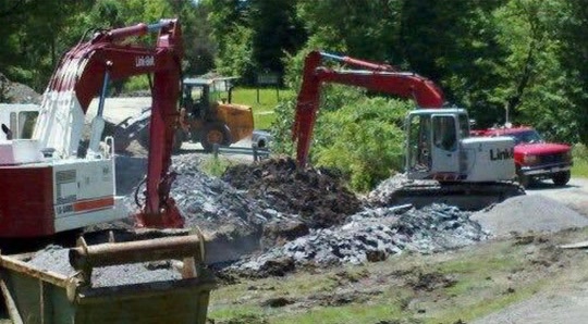 Two tracked excavators and a wheel loader working a demolition spoil pile on a summer jobsite